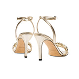 Kibele Sahara Ankle Cross Sandal in shimmering metallic leather, featuring a slender stiletto heel and elegant ankle strap.