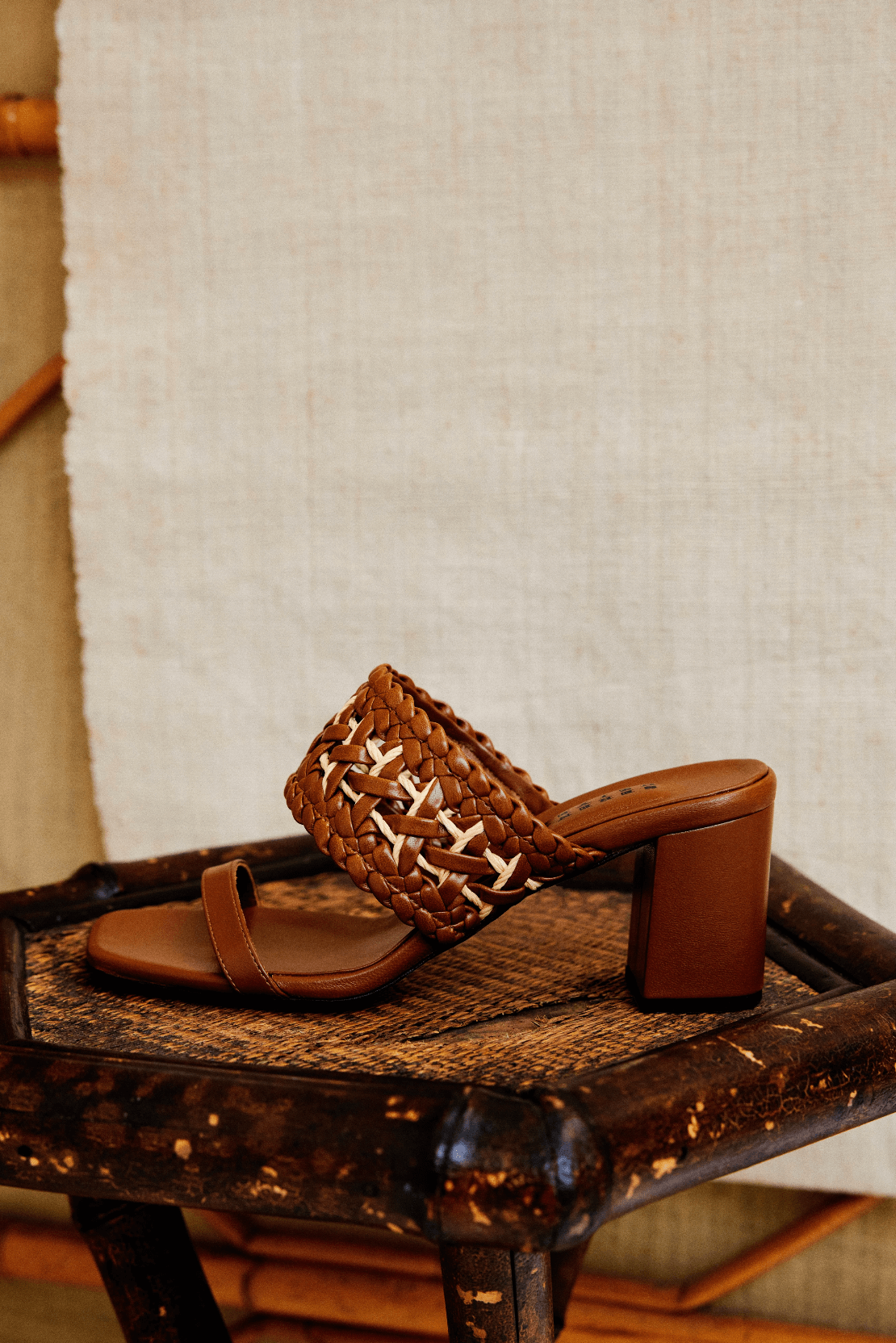 Almeria Camello Block-Heel Strap Sandal, crafted from supple camello leather, displayed on a rustic wooden chair.