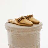 Elegant Catena Gold Sliperette, crafted from metallic leather with a gold and silver chain detail, on a decorative pedestal.
