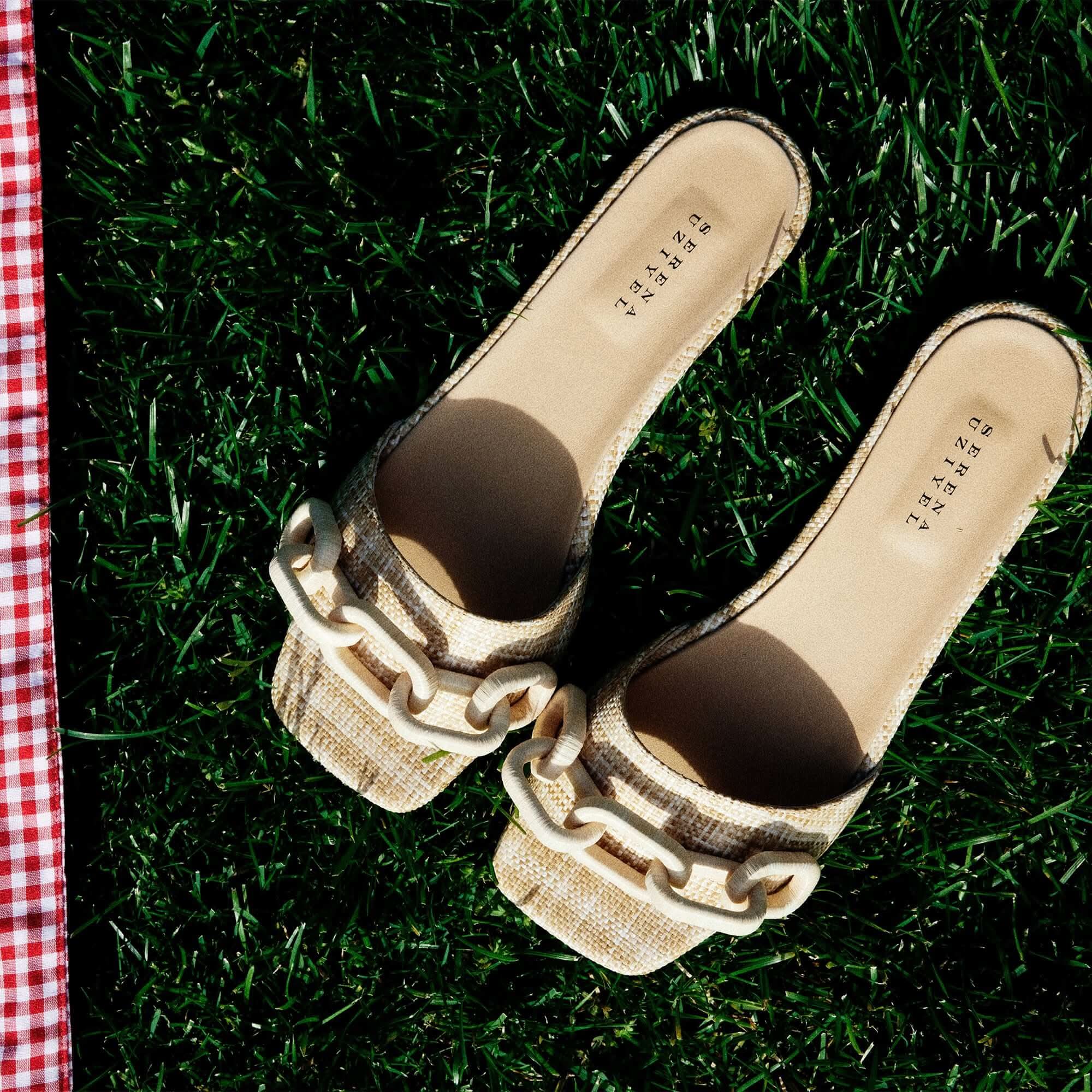 Catena Legno flat sandals featuring natural raffia and chain-shaped embroidery on a grassy background.