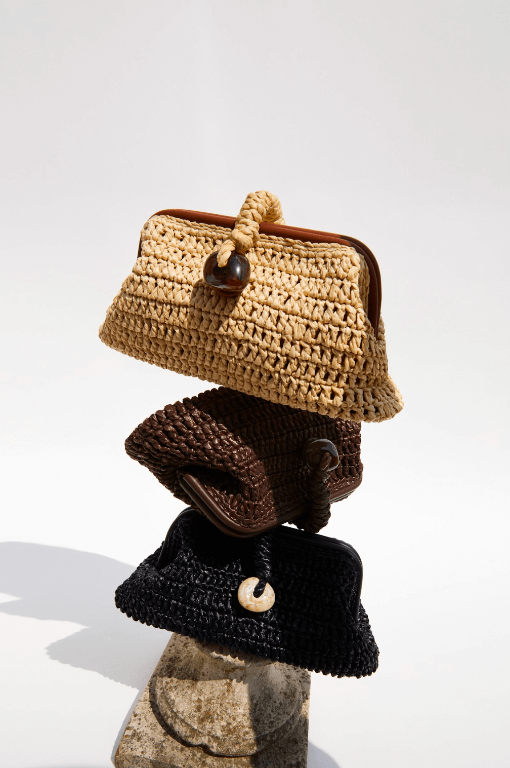 Stack of three artisan-crafted pouch bags made from natural raffia in umber tones.