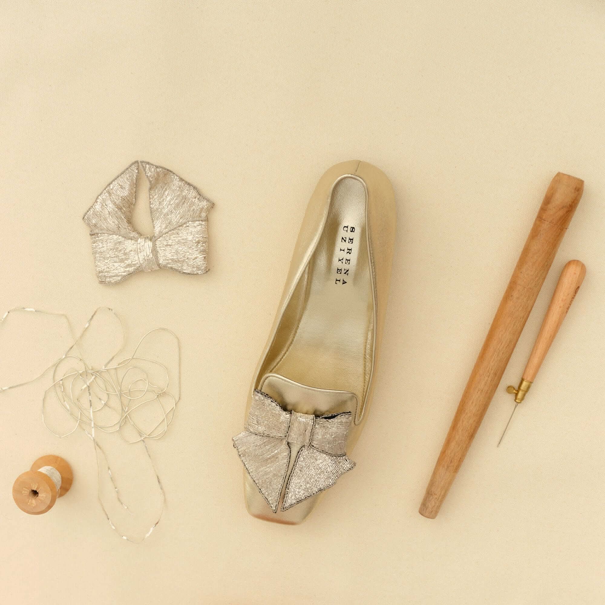 Handmade Fiocco Sahara Flat Moccasin with metallic bow and crafting tools on a beige surface.