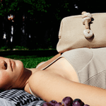 Model relaxing outdoors with Petra Natural Pouch Bag, featuring natural stones and jute rope, embodying Tuscan elegance.