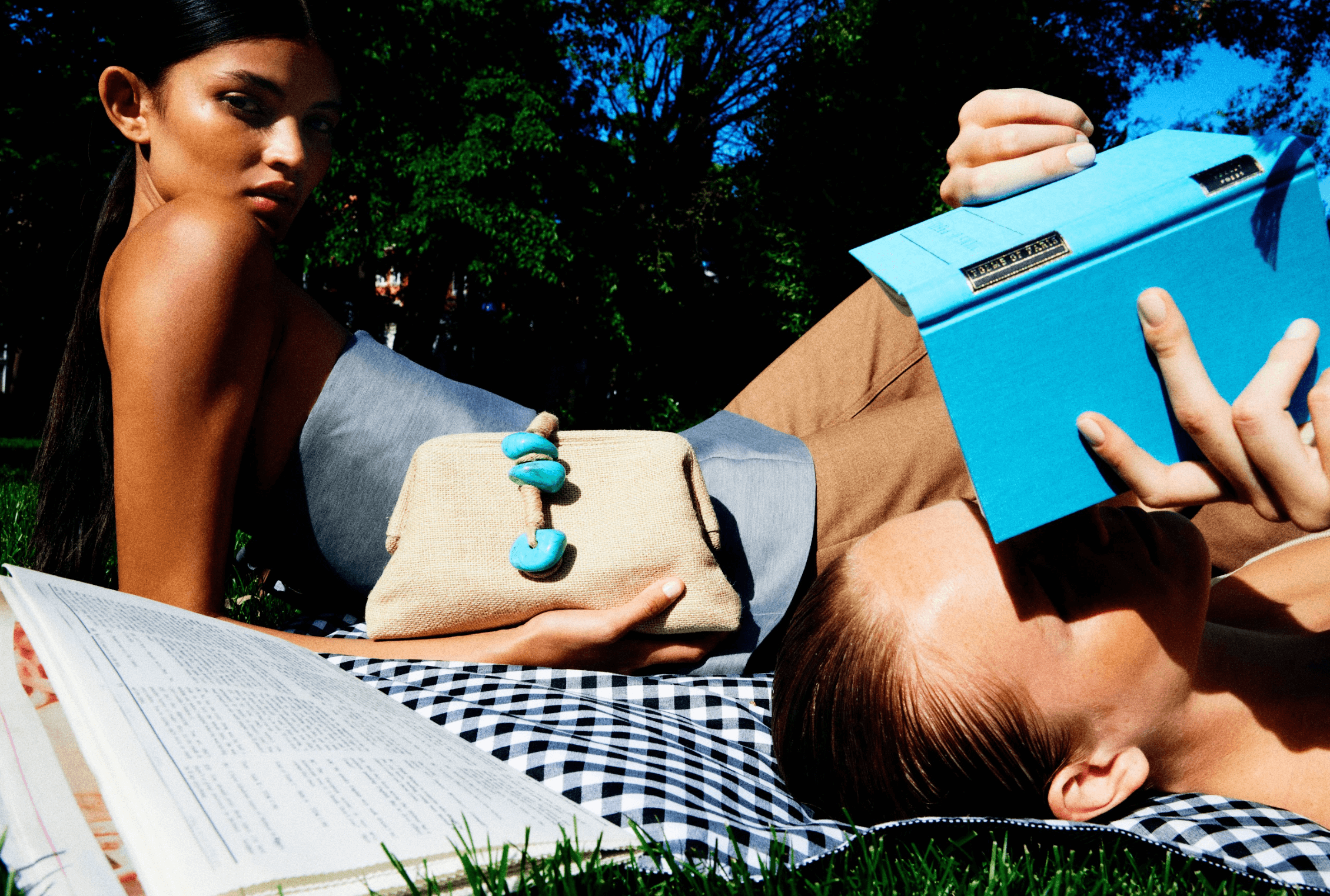 Two models lounging outdoors, one holding a Petra Turquoise Pouch Bag with natural stones, evoking a chic summer vibe.