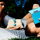 Two models lounging outdoors, one holding a Petra Turquoise Pouch Bag with natural stones, evoking a chic summer vibe.