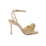 Rhea Gold Ankle Cross Sandal featuring metallic leather and a knotted crochet front strap, on a high stiletto heel.