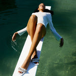 Model relaxing on a float wearing Catena Off-White Flat Sandals, showcasing their elegant design and comfort.
