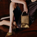 Adia Antique Gold Mini Tote Bag with fringe, elegantly styled with a dress, showcasing versatile fashion appeal.