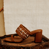 Almeria Camello Block-Heel Strap Sandal, crafted from supple camello leather, displayed on a rustic wooden chair.
