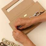 A person placing a card inside a beige clutch with a chain strap, featuring different chain styles beside it.