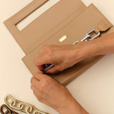 A person placing a card inside a beige clutch with a chain strap, featuring different chain styles beside it.