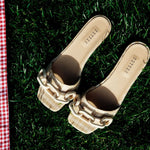Catena Legno flat sandals featuring natural raffia and chain-shaped embroidery on a grassy background.