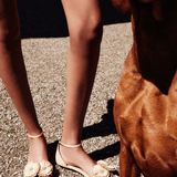 Natural flat ankle sandals adorned with oversized handwoven flowers, showcasing summer style and elegance next to a dog.