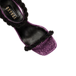Roxana high-heel ankle sandal featuring iridescent leather, purple hue, and intricate raffia braiding details.